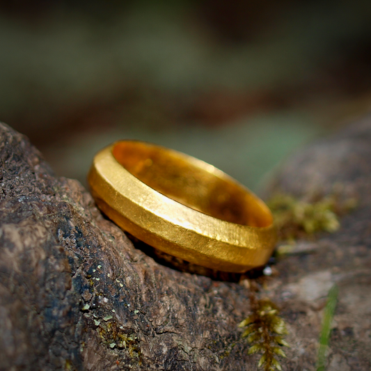 A 3-sided geometric gold band with a textured finish, resting on a rough surface with moss.